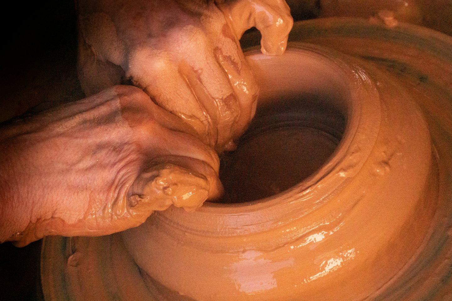 Hands shaping wet clay on a pottery wheel.