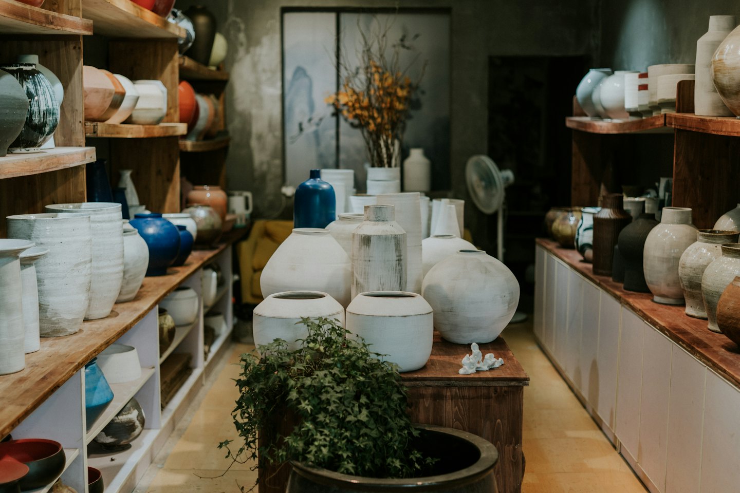 Handmade ceramic pottery displayed on wooden shelves and table.