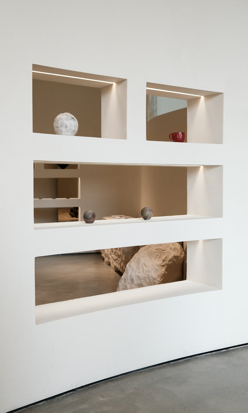 White wall with illuminated niches displaying art objects.