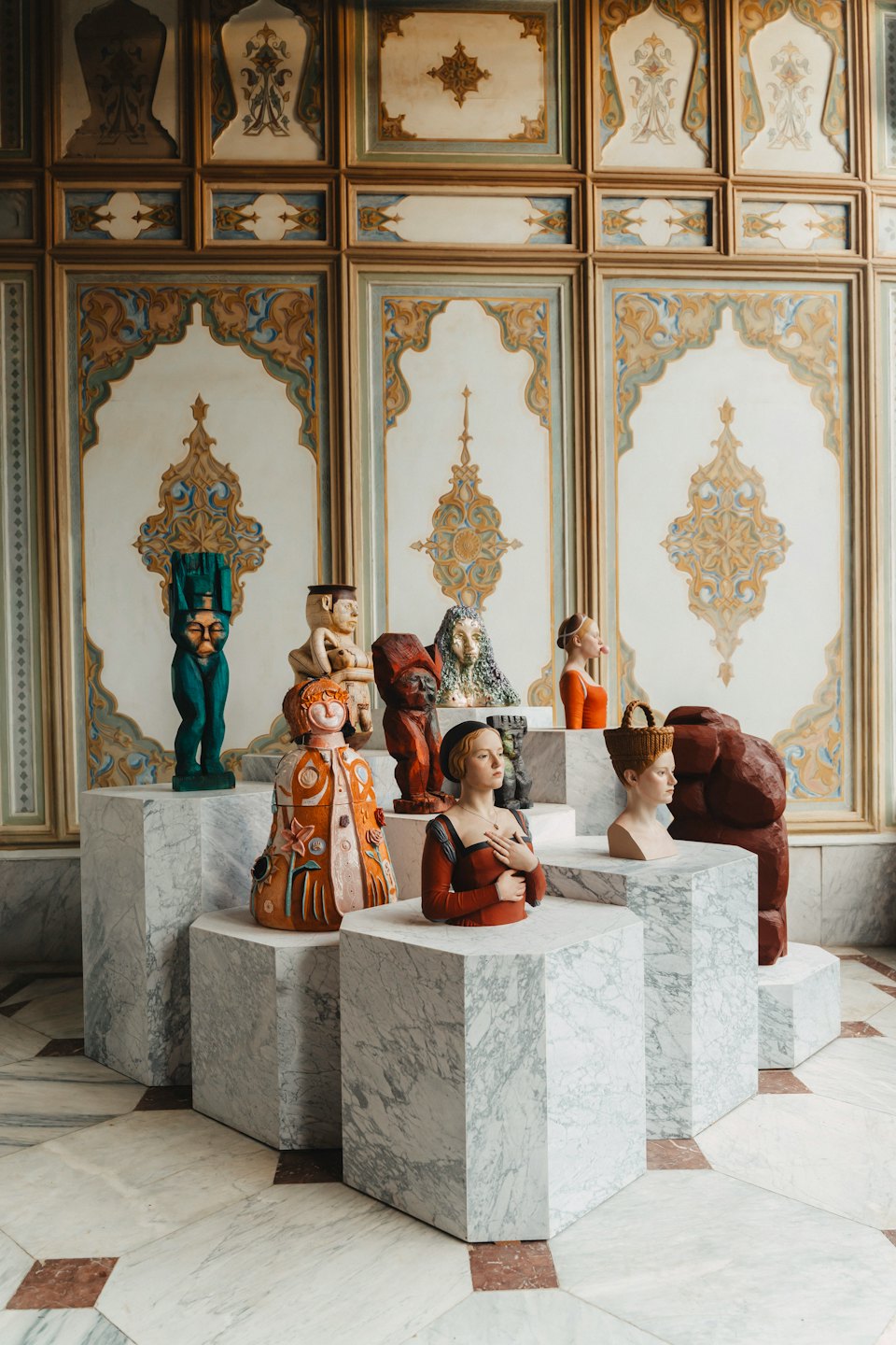 Ceramic and wooden sculptures displayed on tiered marble pedestals.